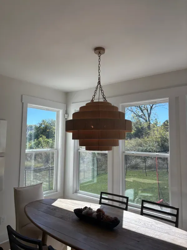Dining room with a wood pendant light, oval table, and large windows overlooking a backyard.