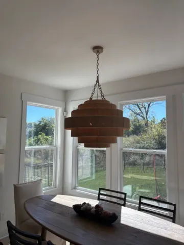 Dining nook with a wooden table, modern pendant light, and large windows overlooking a grassy yard