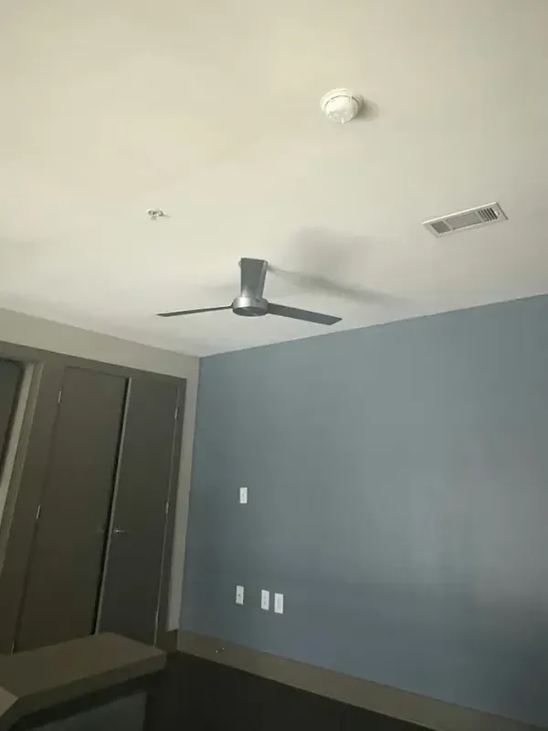 Empty bedroom with a ceiling fan, gray-blue wall, and dark closet doors