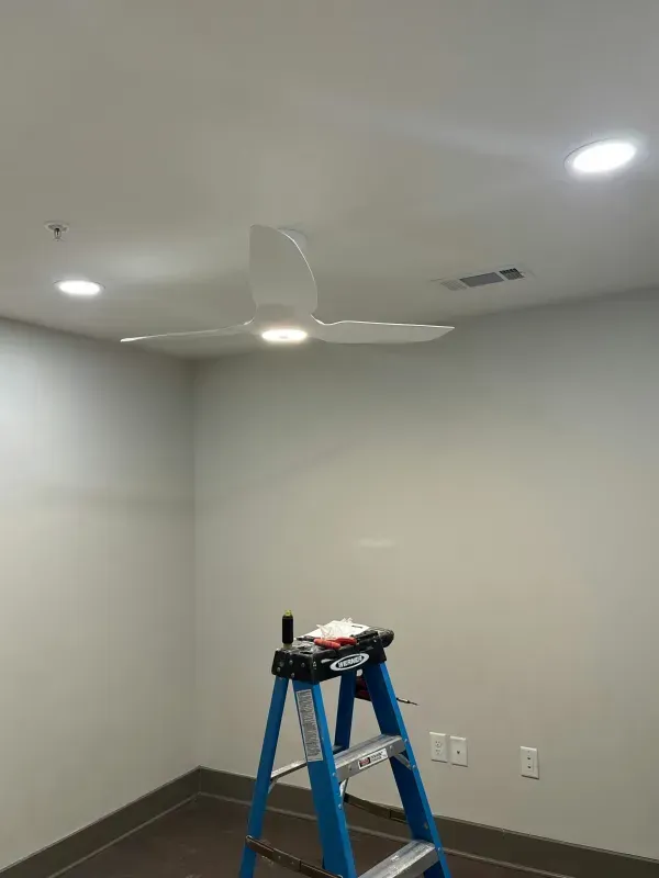 Empty room with white walls, ceiling fan, recessed lights, and a blue step ladder near the corner.