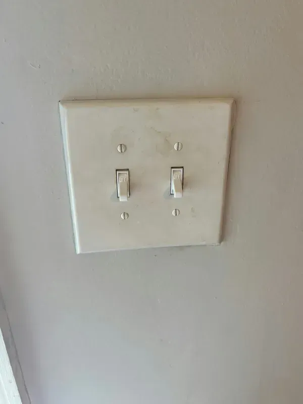Two white toggle light switches on a beige wall plate.