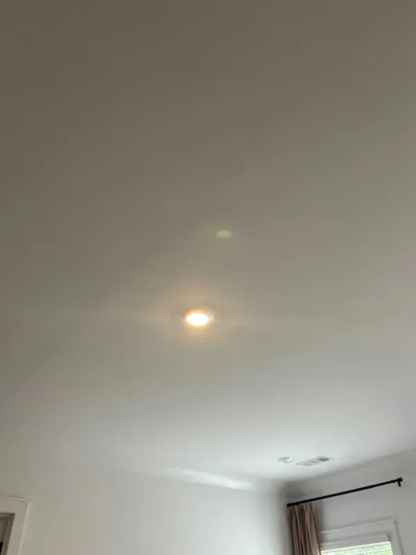 Ceiling light on a white room ceiling with a small green lens flare near it.