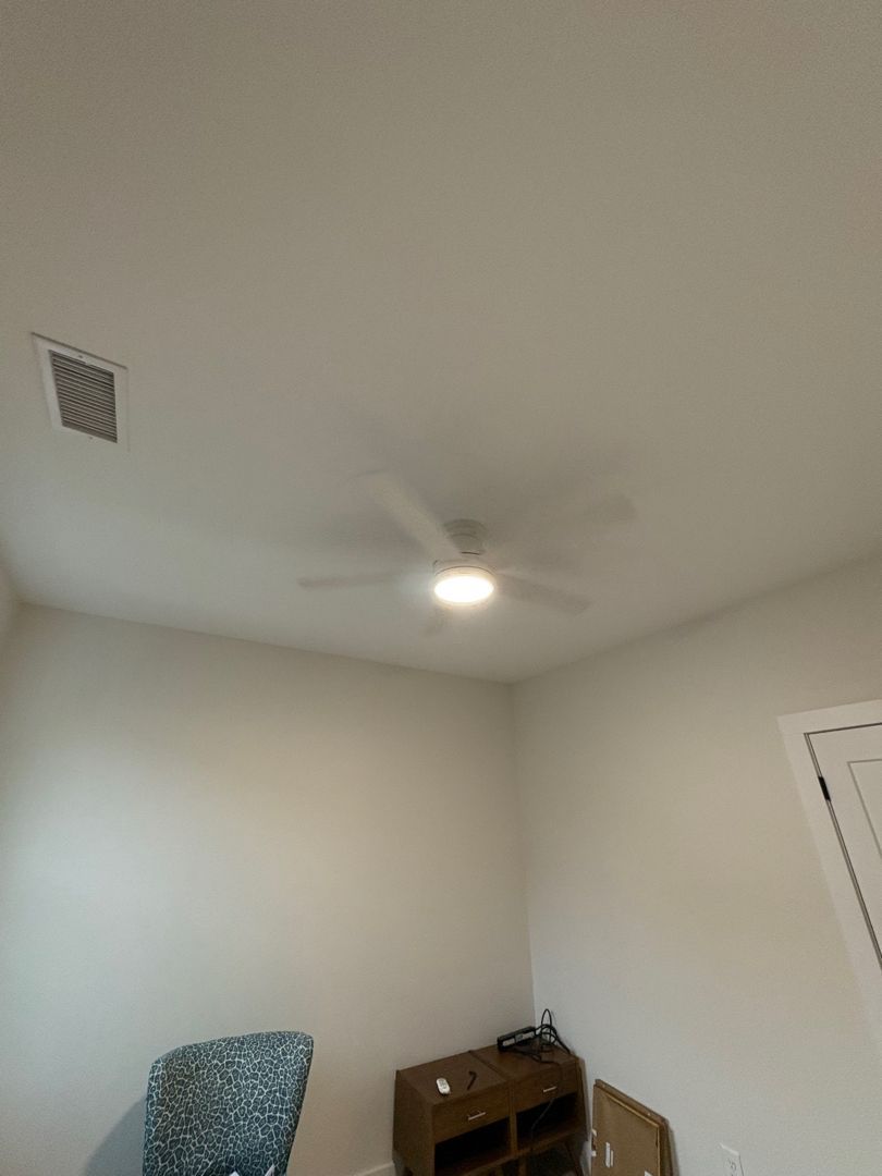 Empty bedroom corner with white walls, ceiling fan light, chair, and small wooden dresser