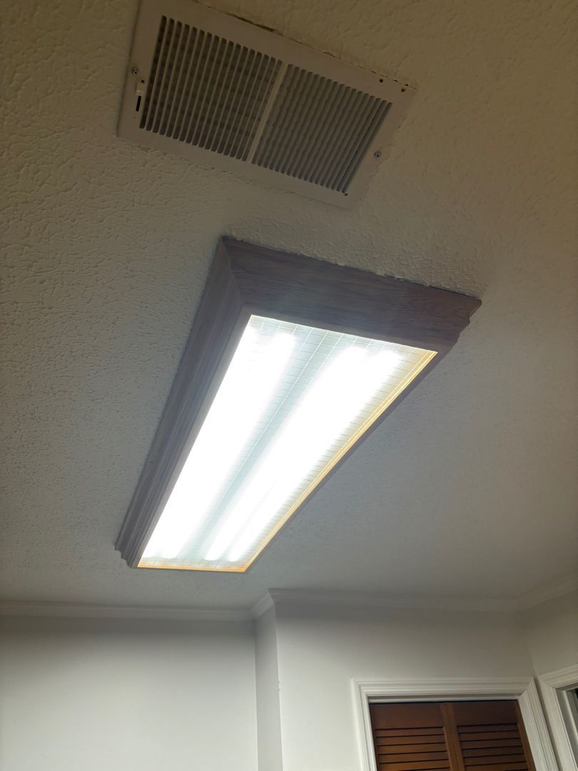 Ceiling with fluorescent light fixture and air vent in a room, seen at an angle.