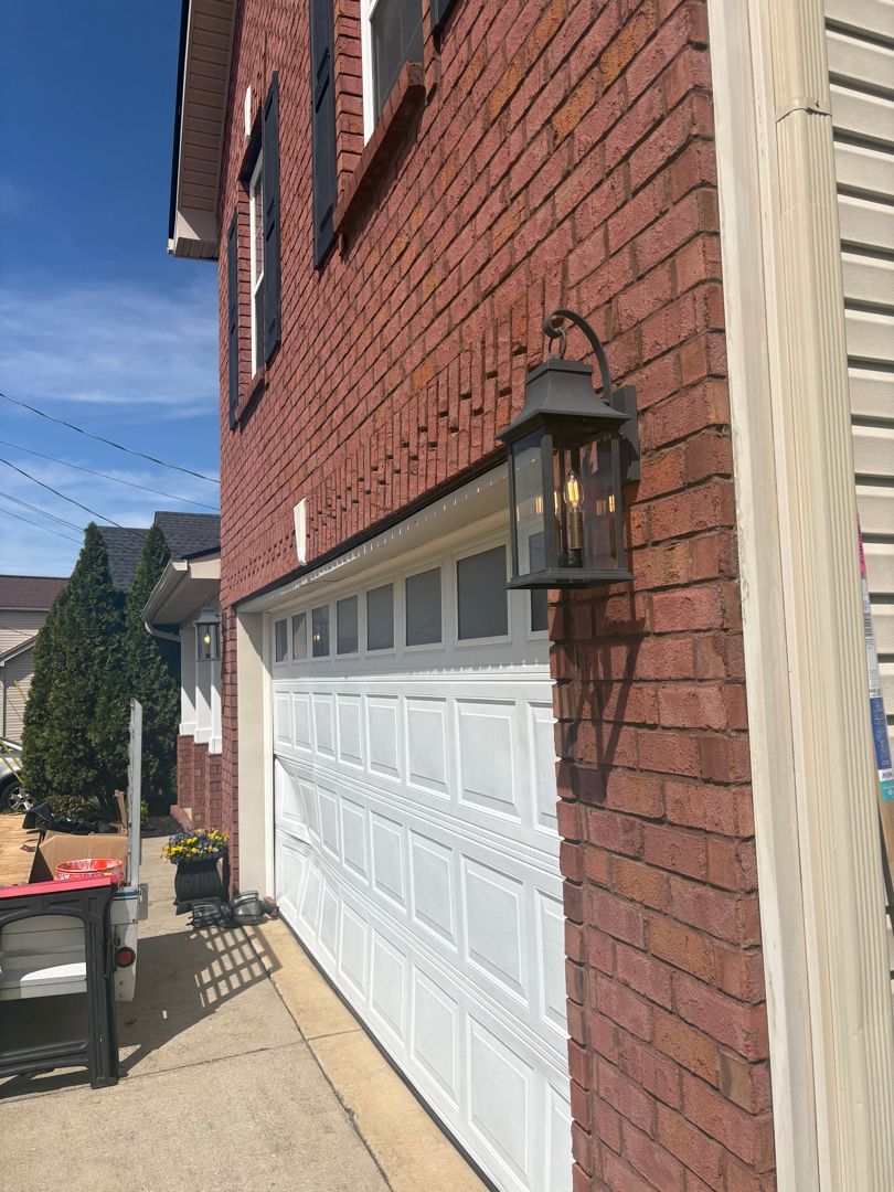 Red brick house exterior with white garage door and wall-mounted lantern light.