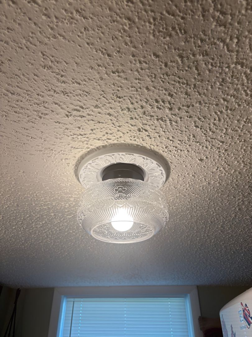 Ceiling light fixture on a textured white ceiling above a window with blinds