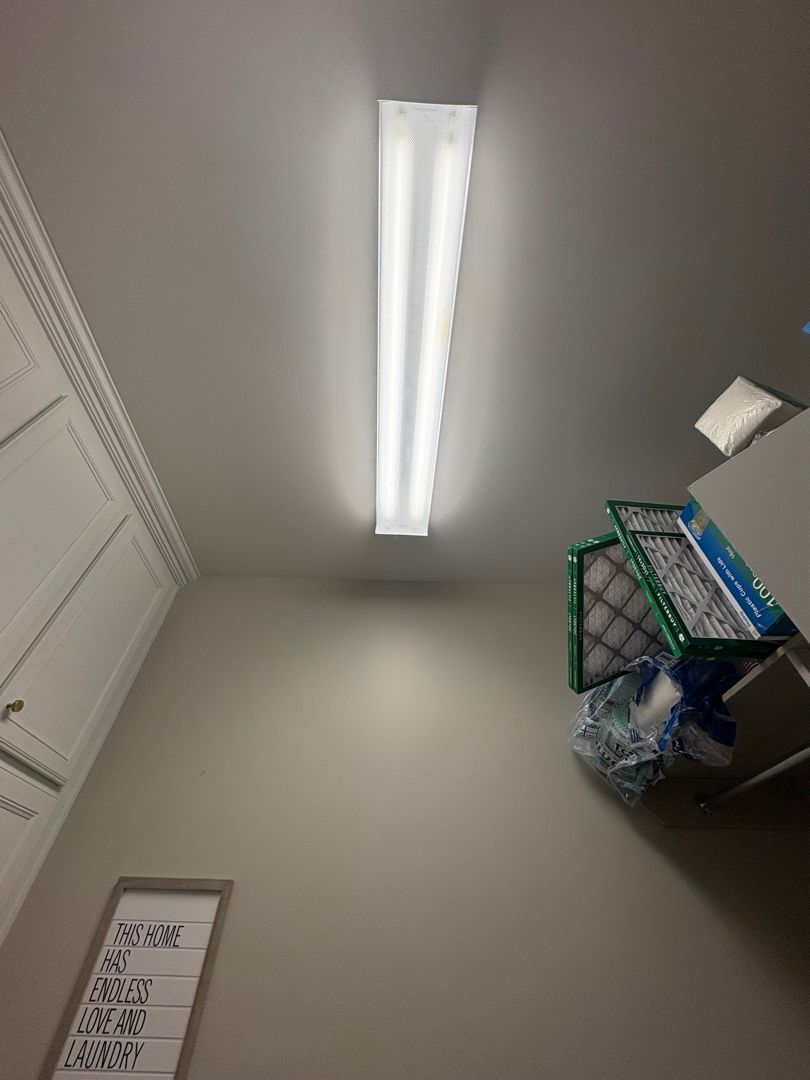 Ceiling view of a small room with fluorescent lights, wall sign, and a shelf with supplies in the corner