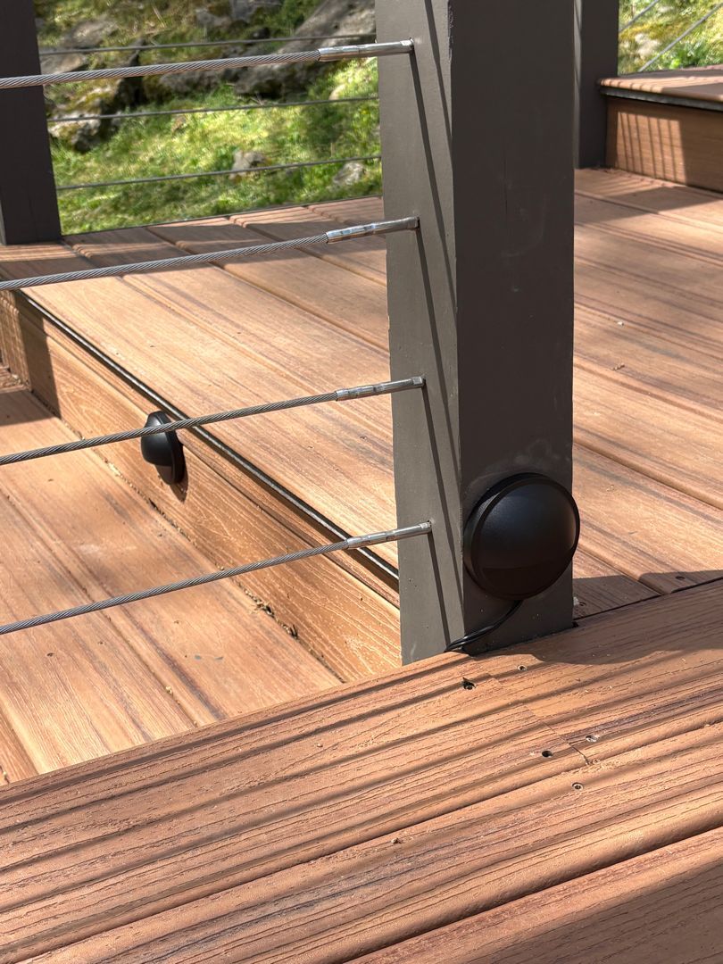 Wooden deck with cable railing and a black post cap beside steps in a sunlit outdoor setting