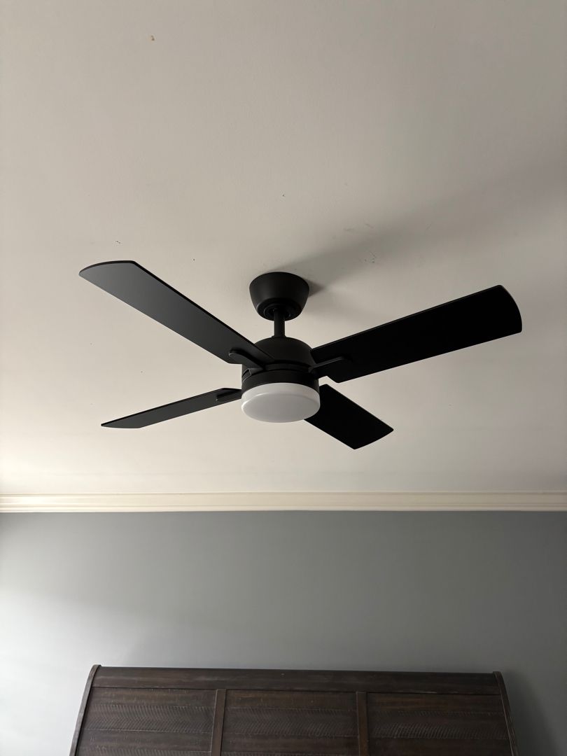 Black ceiling fan with light on a white ceiling above a wooden headboard.