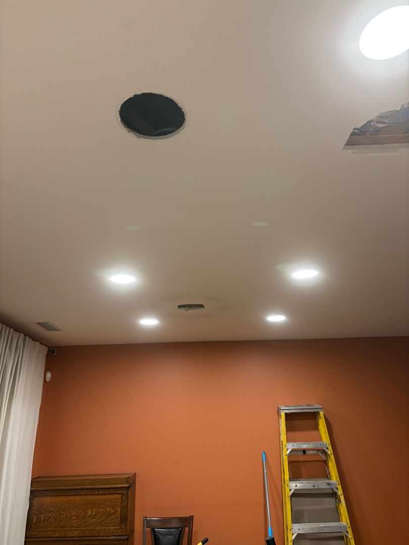 Ceiling with recessed lights, black vent, and a yellow ladder against an orange wall.