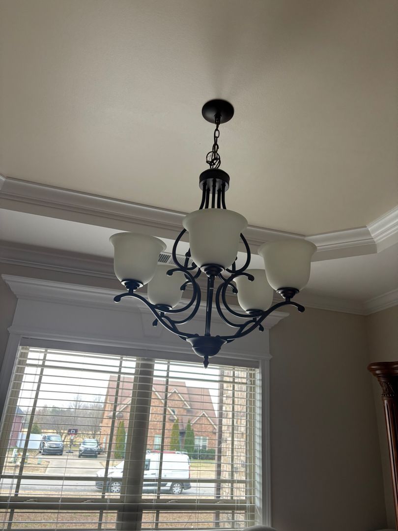 Black chandelier with frosted glass shades hanging in a room above a window with blinds