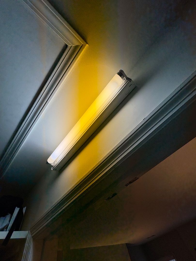 Fluorescent ceiling light fixture glowing on a white ceiling with a warm yellow tint.