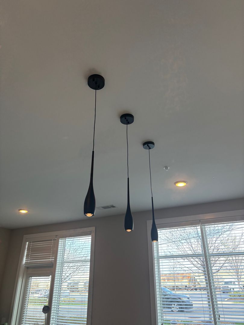 Three black pendant lights hang from a white ceiling above windows with blinds.