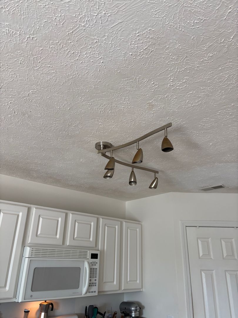 Kitchen ceiling light fixture with three adjustable spotlights above white cabinets and a microwave