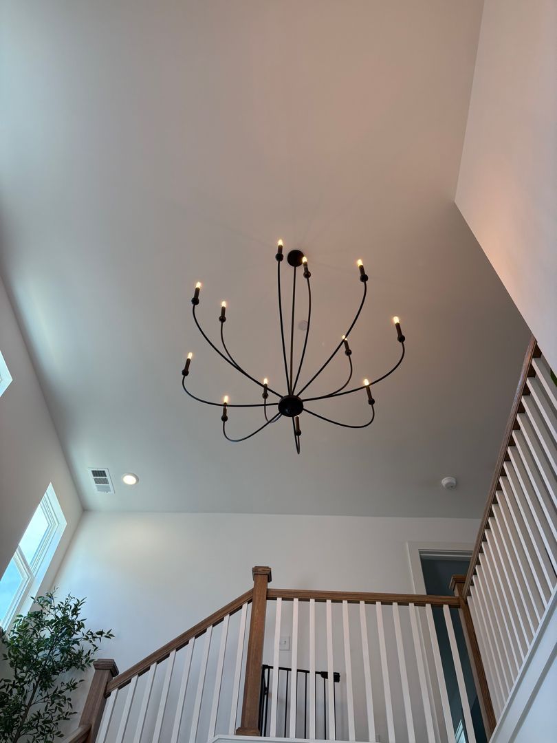 Staircase with white railings under a black chandelier in a bright interior foyer
