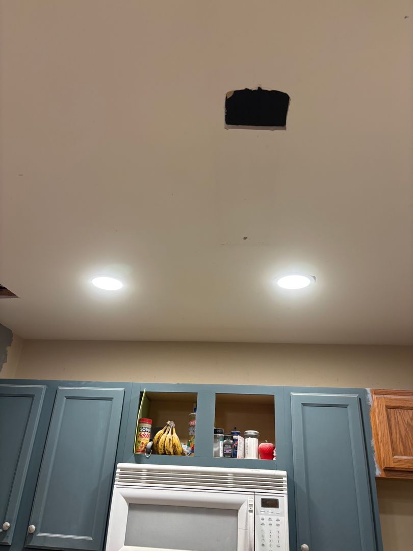 Kitchen ceiling with a black vent opening above blue cabinets and a microwave.