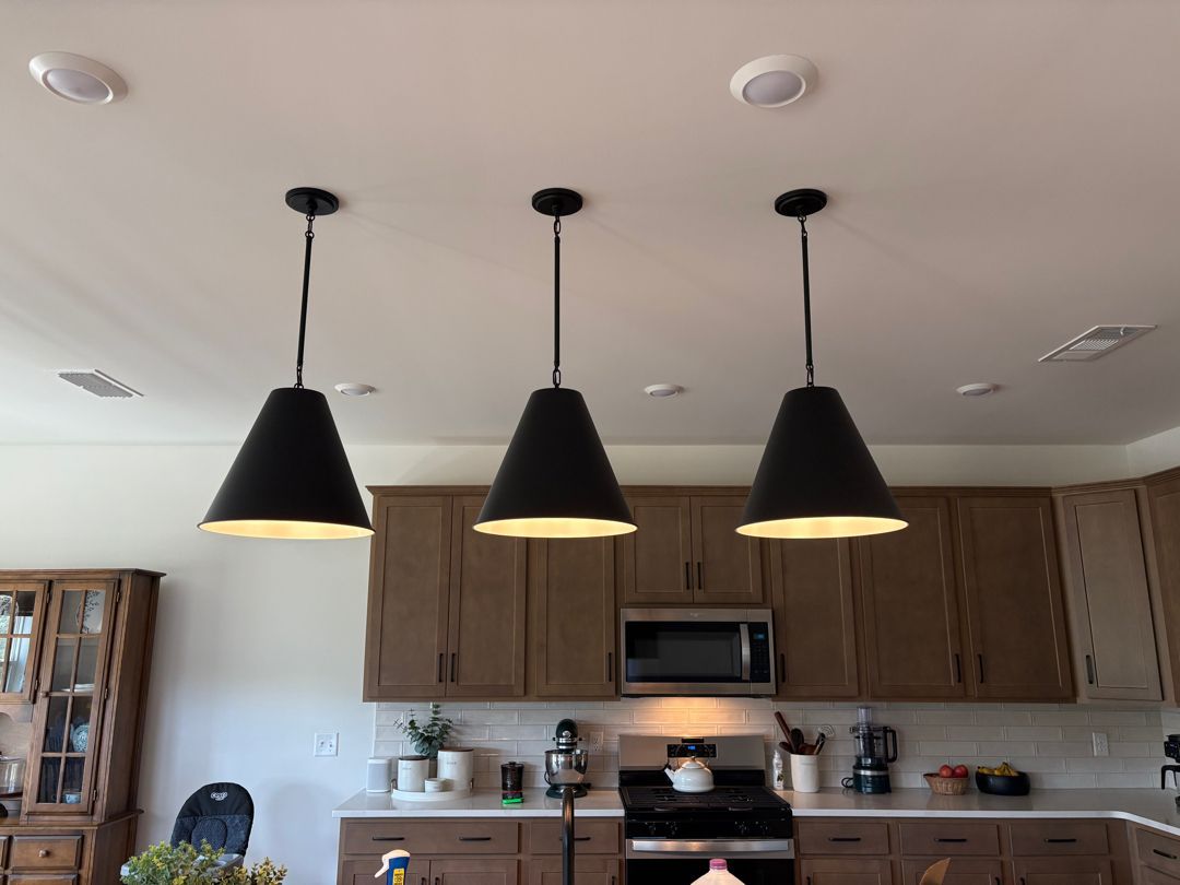 Modern kitchen with three black pendant lights over a counter and wood cabinets behind.