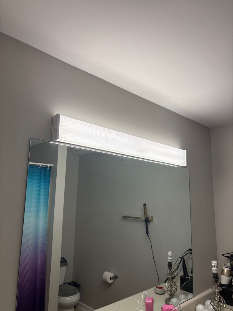 Bathroom mirror with bright light fixture above and a shower head reflected below.