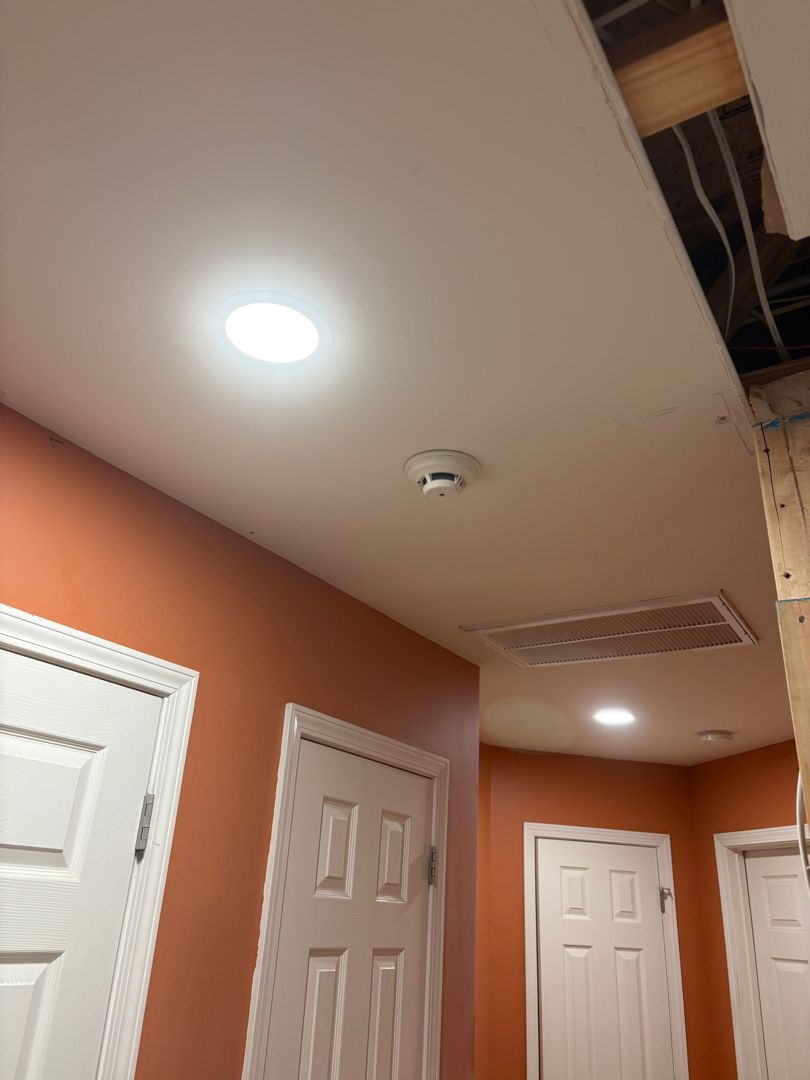 Hallway with orange walls, white doors, ceiling lights, and an open ceiling panel exposing wiring