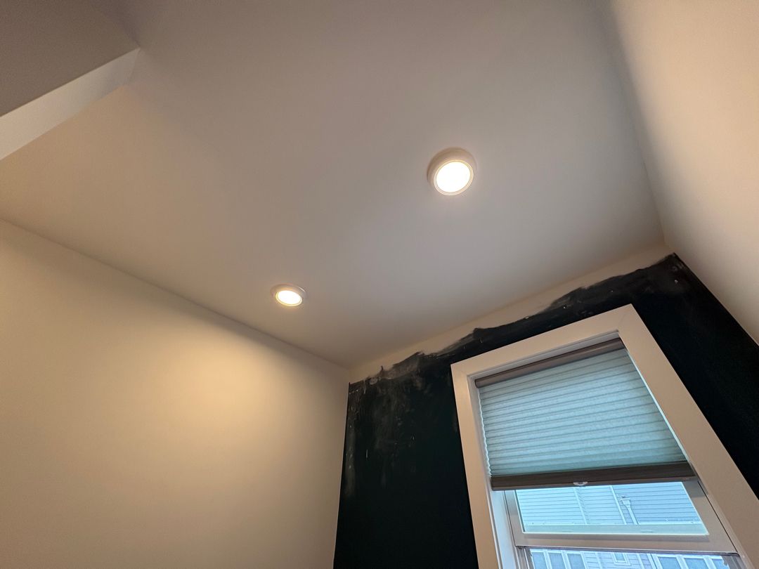 Ceiling corner with two recessed lights and a window with blinds and dark curtains