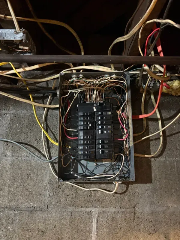 Open electrical panel with tangled wires on a cinder block wall