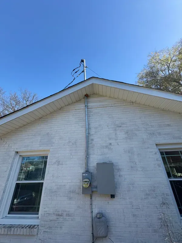 Side of a white house with a utility meter, downspout, and two windows under a blue sky