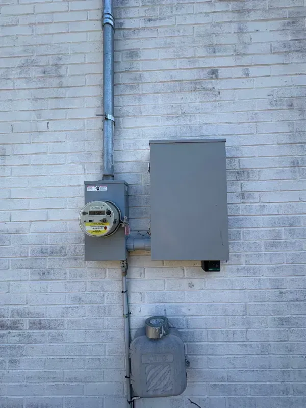 Two utility meters mounted on a white brick wall, one gray box and one with a yellow dial.