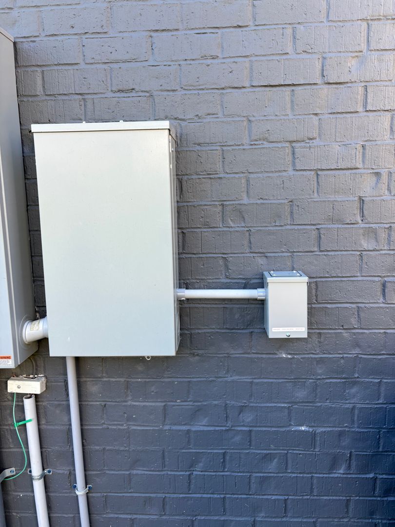 White electrical boxes and conduit mounted on a gray brick wall