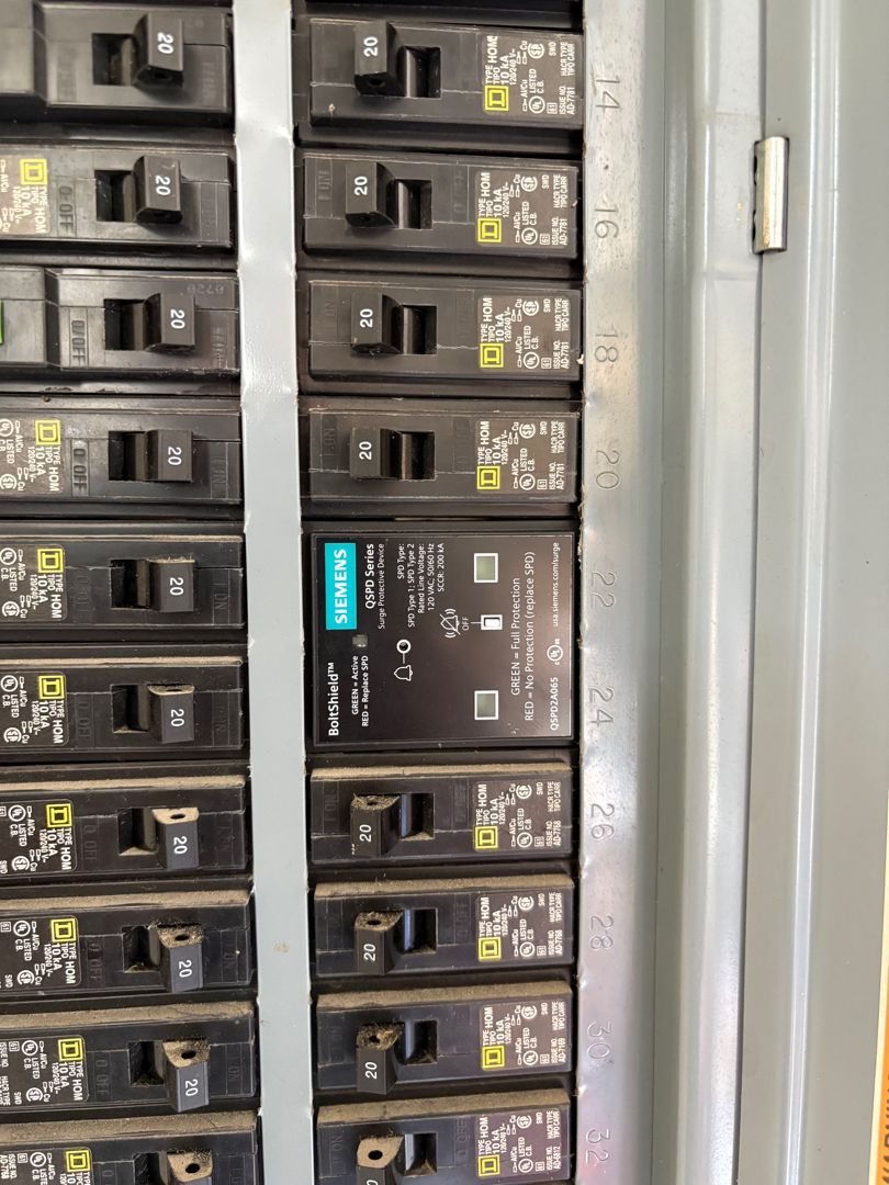 Open electrical breaker panel with rows of black circuit breakers and a gray door frame