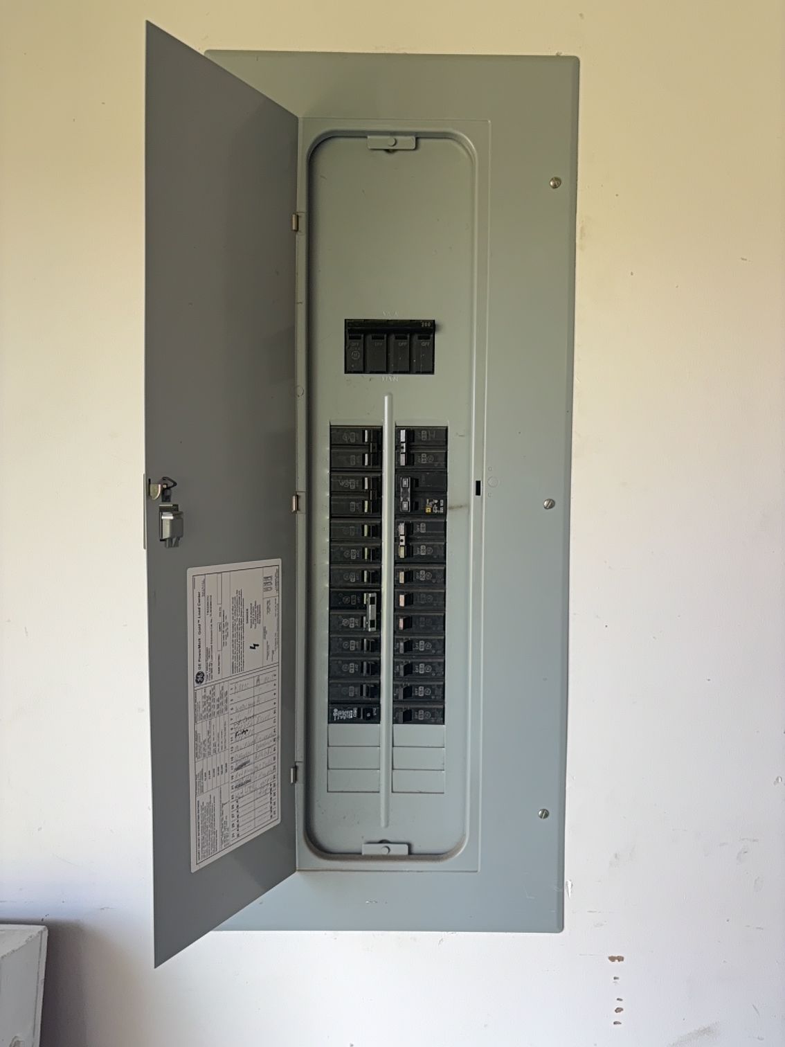 Open electrical breaker panel with door ajar on a white wall