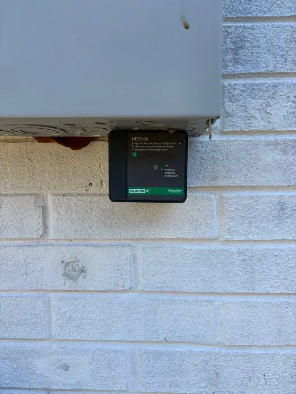 Small black electronic device mounted under a metal box on a white brick wall