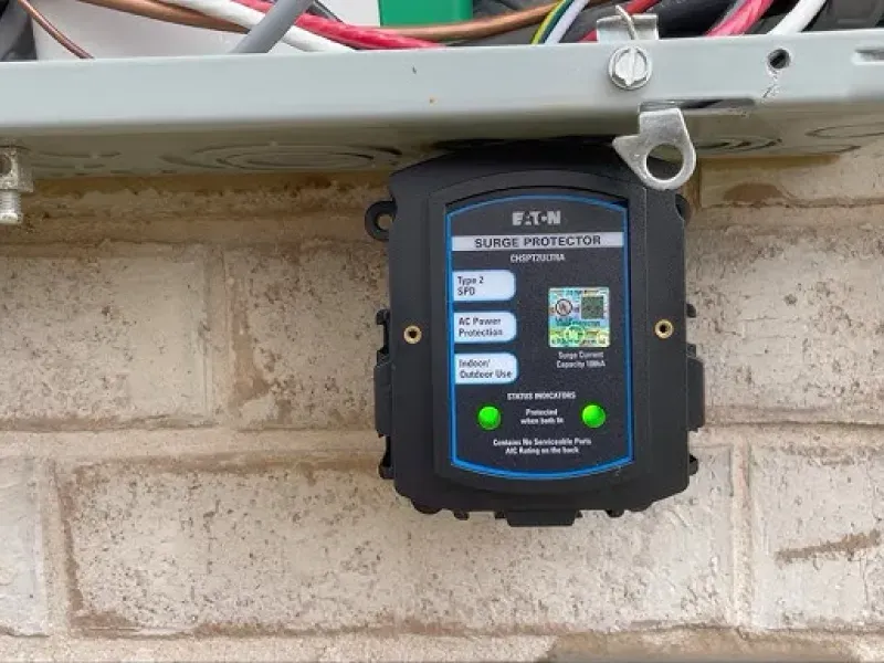 Black electronic control box with blue label mounted on a brick wall beneath wiring and conduit.