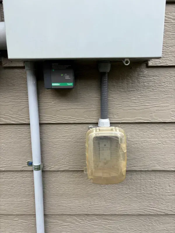 Outdoor utility box with a small black device and a hanging translucent container on a wall.