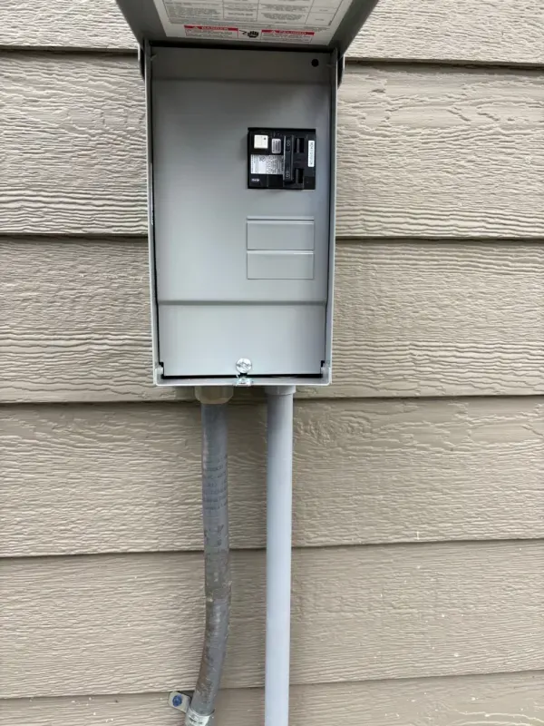 Open electrical meter panel on beige exterior wall with conduit and wires visible