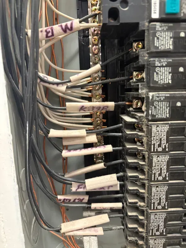 Electrical breaker panel with multiple labeled white wires connected to a row of black breakers.