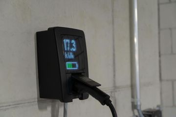 Wall-mounted black digital meter with glowing blue display and a plugged-in cable in a tiled room