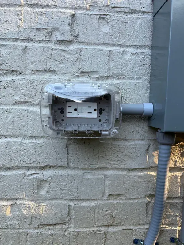 Outdoor brick wall with a damaged electrical outlet box and exposed wiring conduit