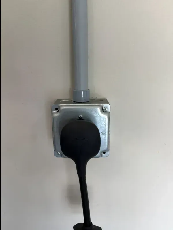 Black cable plugged into a wall outlet with a gray conduit above it.