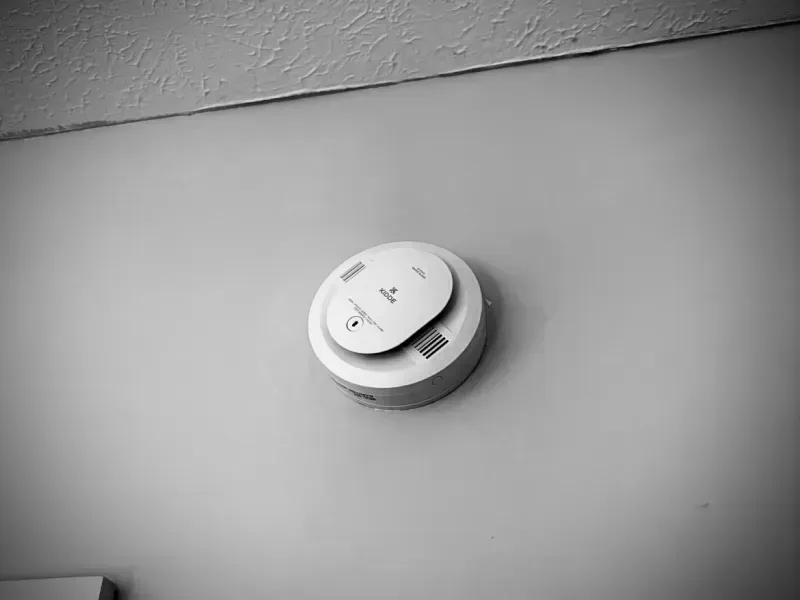 White smoke detector mounted on a ceiling near a wall corner