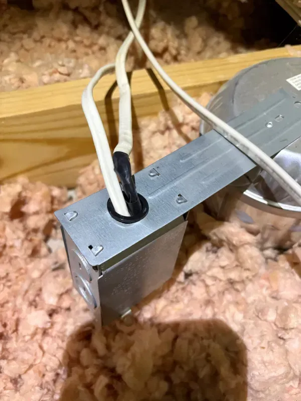 Metal electrical junction box in attic insulation with white wires entering through a black grommet.