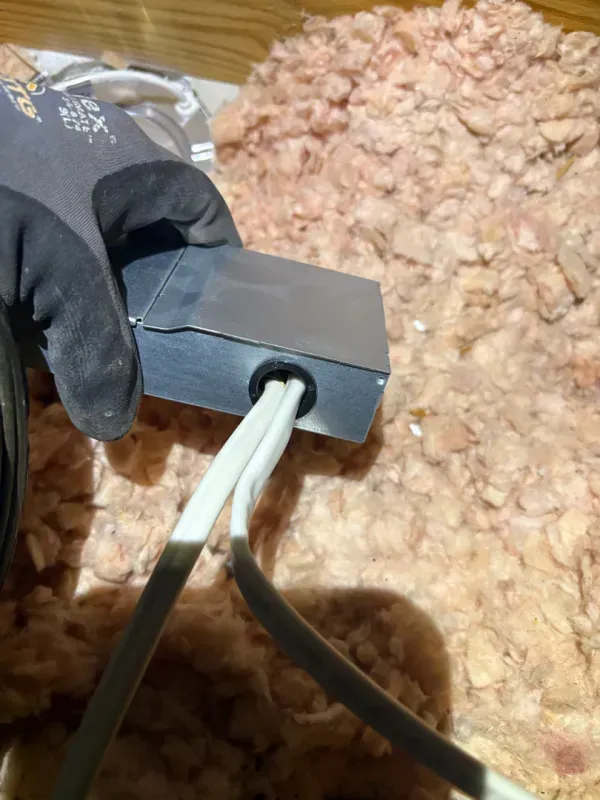 Gloved hand holds a black cable gland with white wires against a pile of pink insulation.