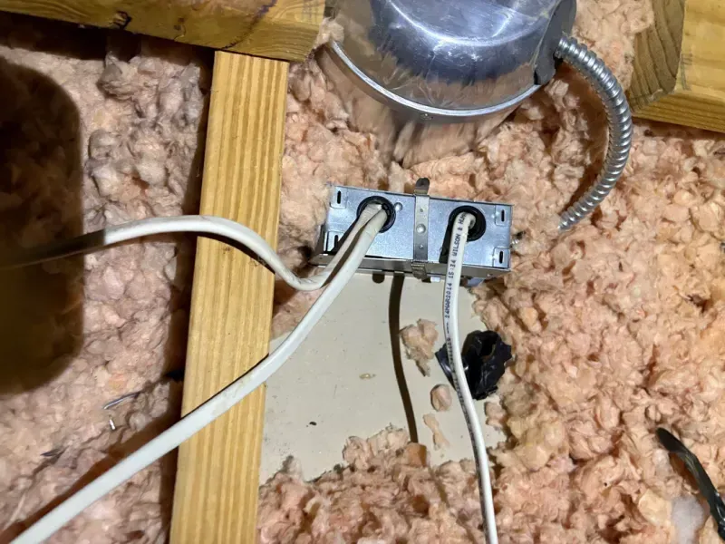Two white cables connected to a metal junction box on exposed insulation in an attic