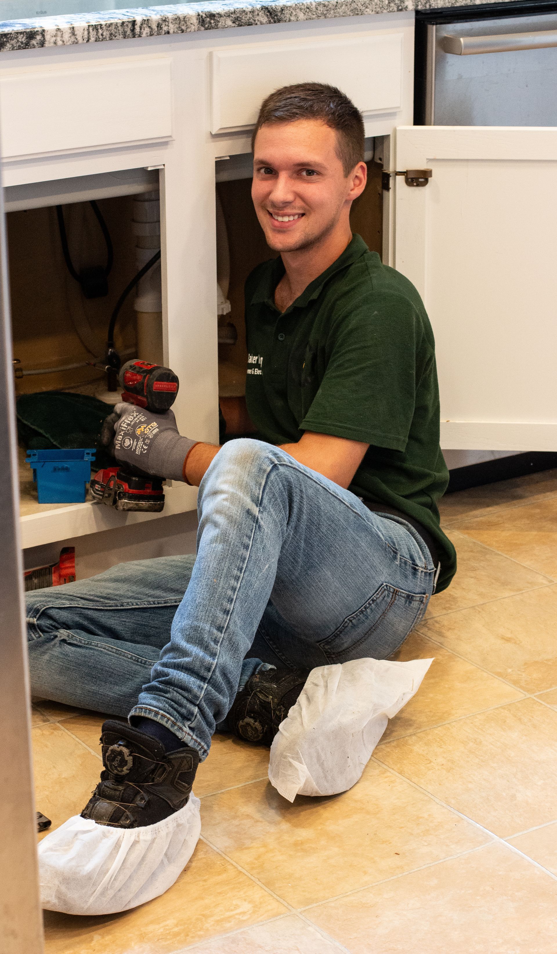 Person kneeling on a floor in a workshop, smiling and holding a small tool near a cabinet.