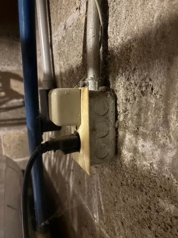 Close-up of electrical outlets and plugged-in cords on a concrete wall