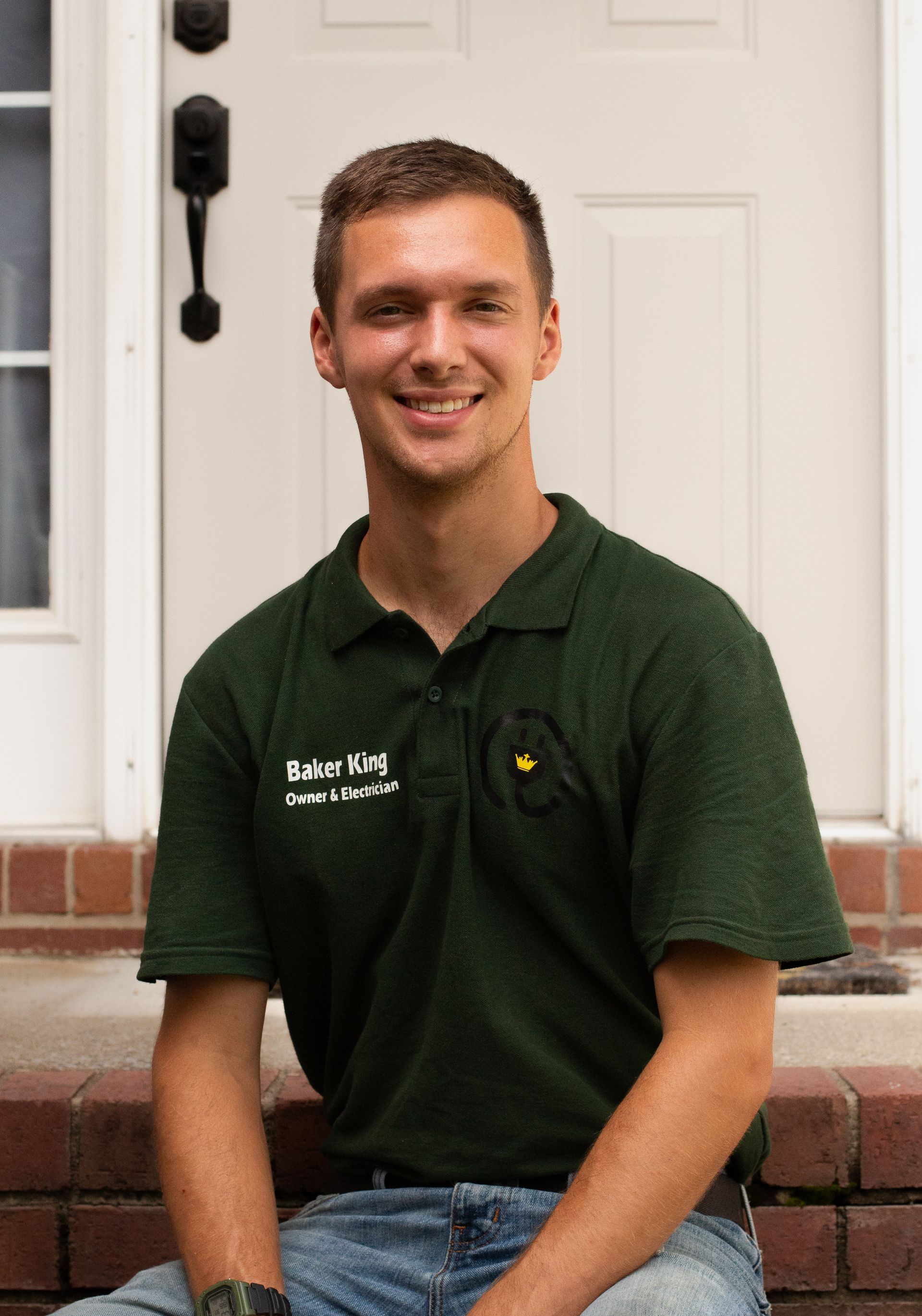 Smiling person in a dark green polo shirt sitting on brick steps in front of a white door