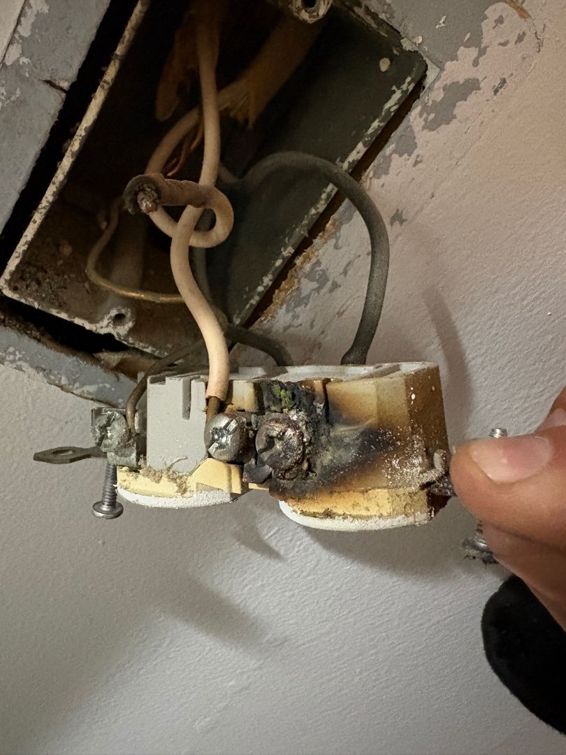 Burned electrical outlet wiring being held up near a wall opening