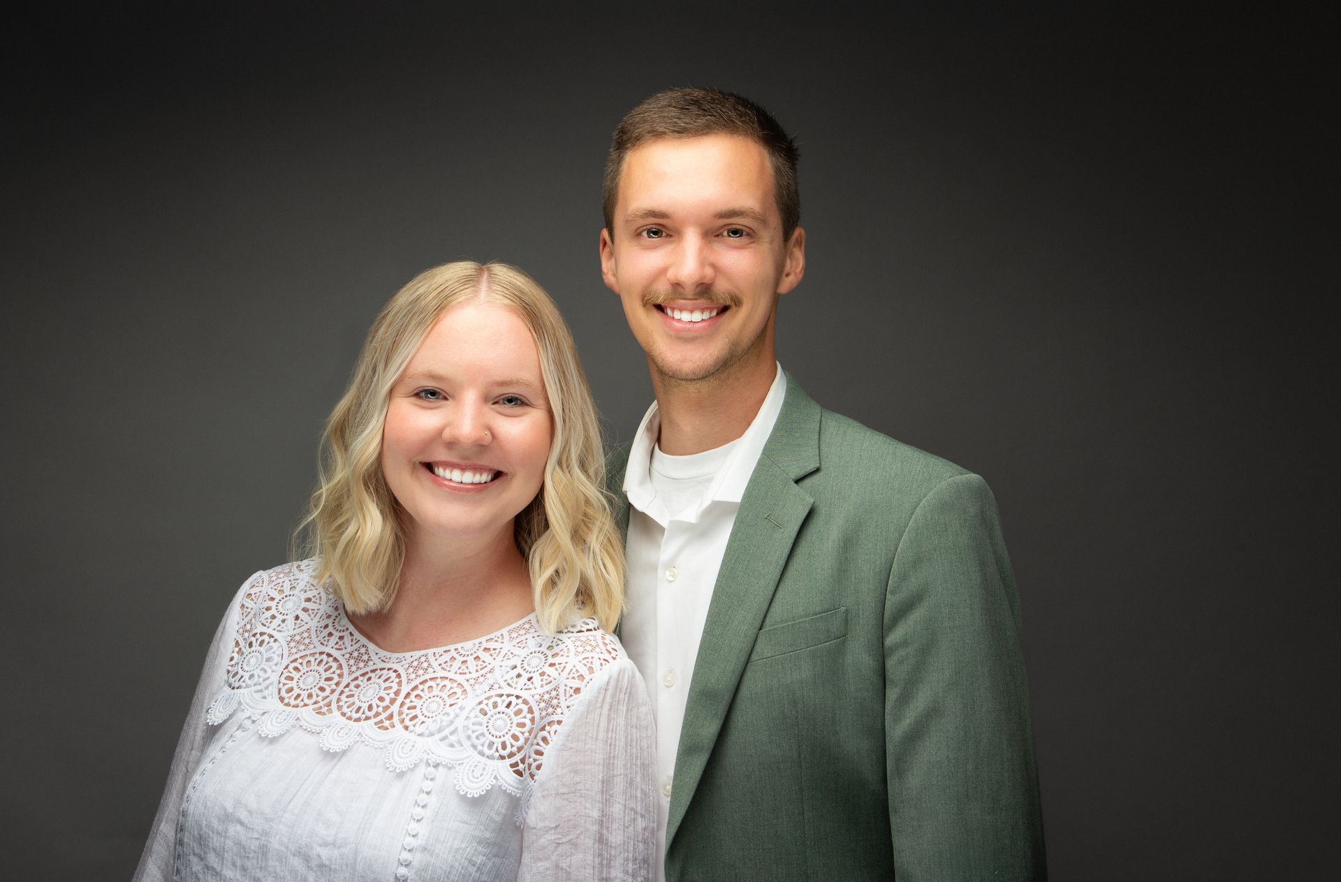 Smiling couple posing against a dark studio backdrop, wearing white and green clothing.