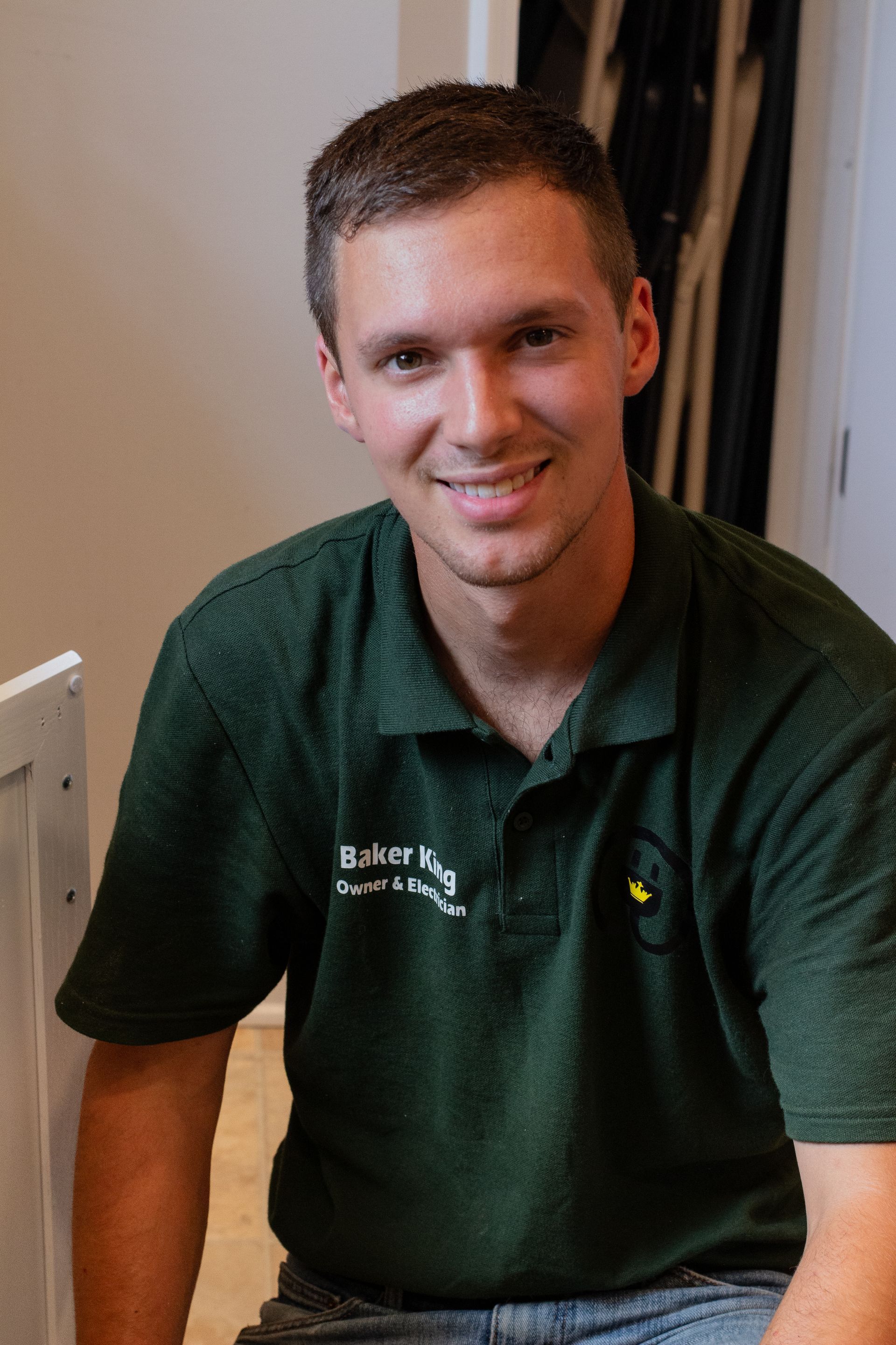 Smiling man in a green polo shirt leaning against a wall indoors.