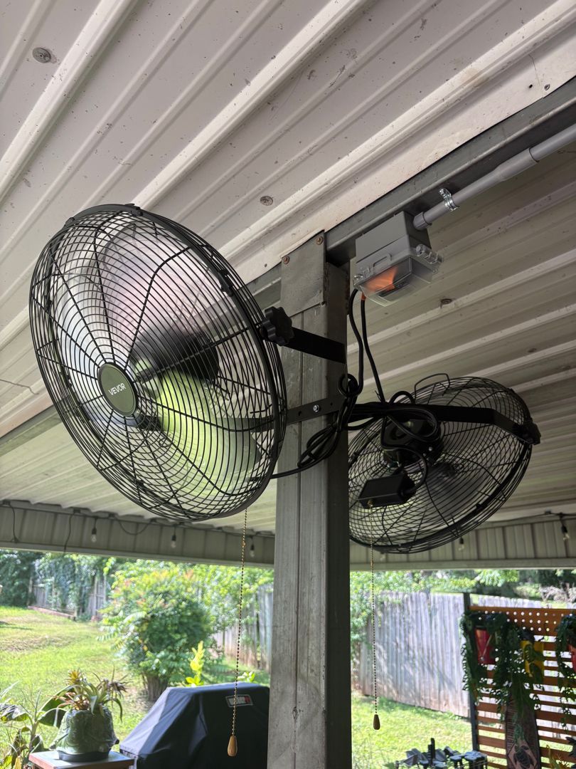 Two black wall-mounted fans under a patio roof, with one fan spinning