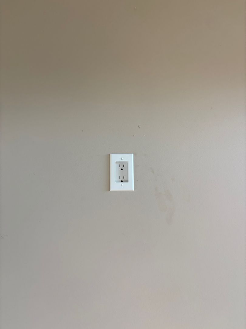 Beige wall with a small white electrical outlet plate centered on it
